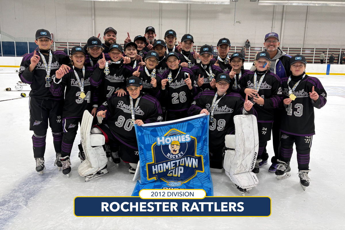 Hockey team posing with a banner on an ice rink, wearing black and purple uniforms.
