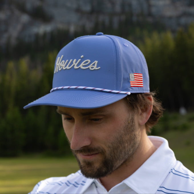 Man wearing a blue cap with 'Howies' branding and an American flag patch outdoors.