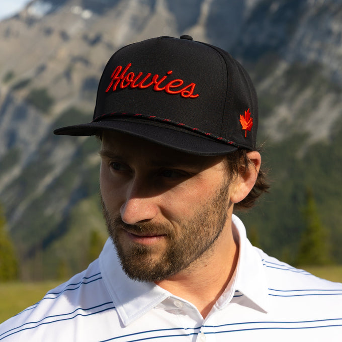 Man wearing a black cap with 'Howies' logo in red against a mountainous background