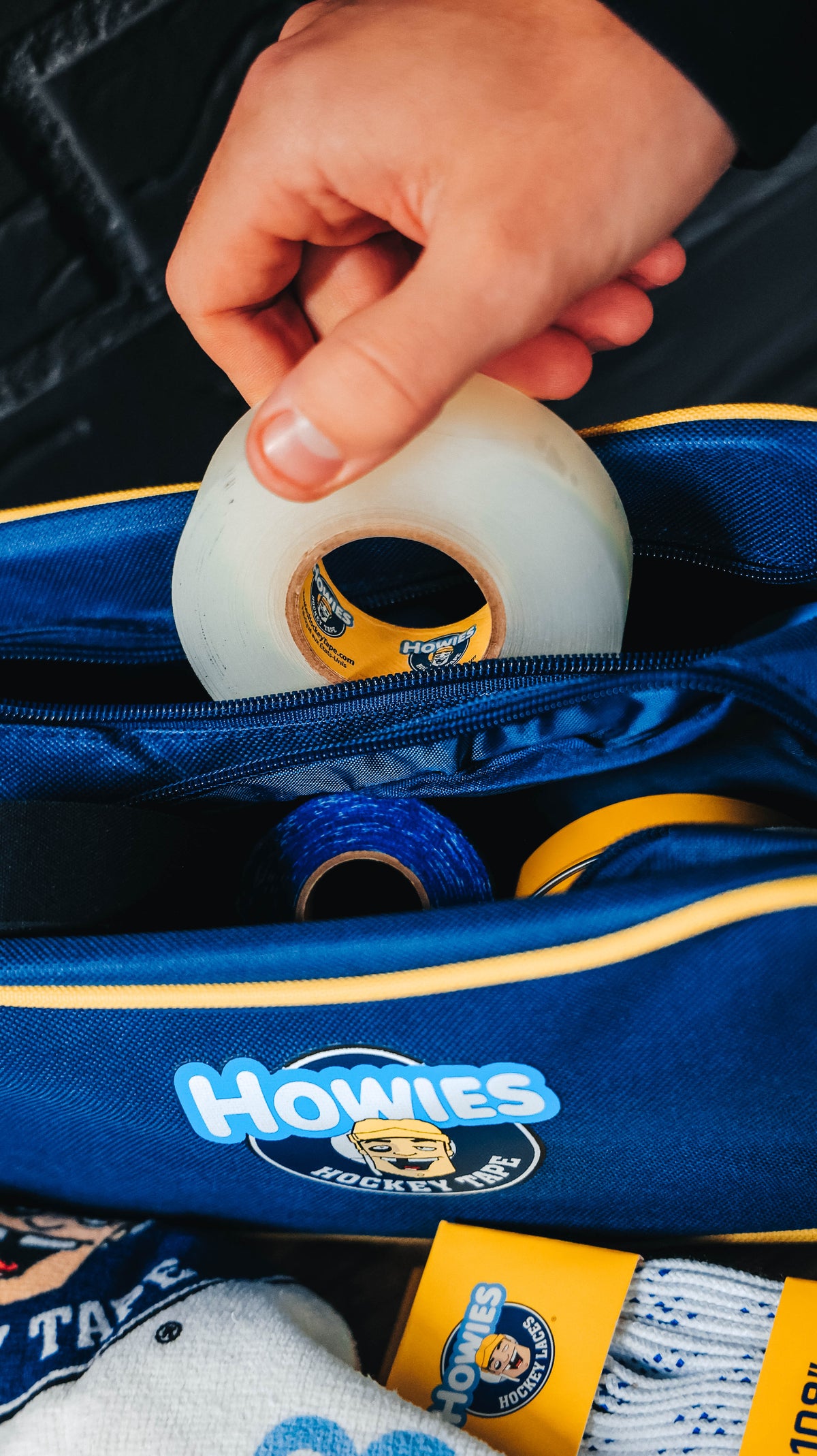 Hand reaching into a Howies hockey bag with hockey tape and equipment.