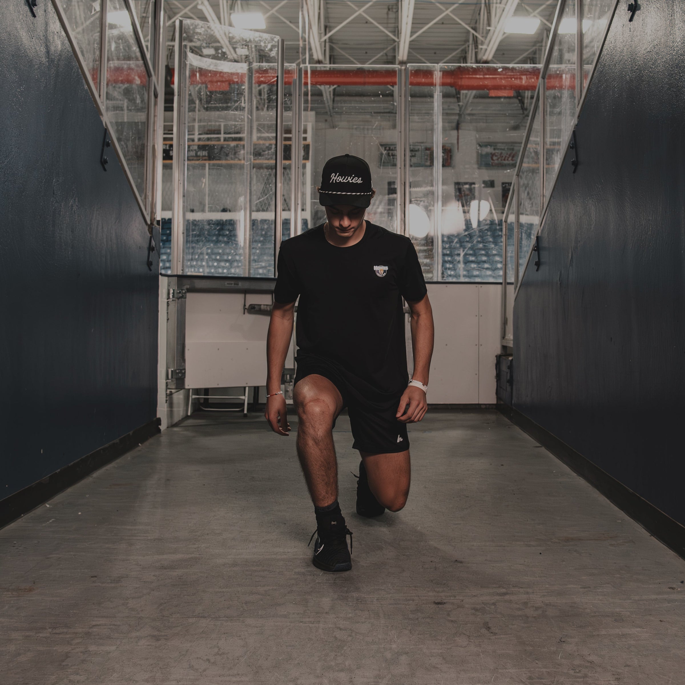 Person in black athletic wear and howies tour lid doing lunges in a hockey rink