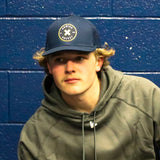 Person wearing a cap and hoodie against a blue brick wall