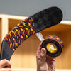 A person holds a hockey stick and a roll of hockey tape with a black, red, and yellow flame pattern in front of a wooden storage cubby wall.