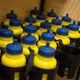 Yellow bottles with blue lids in a holder against a tiled wall.