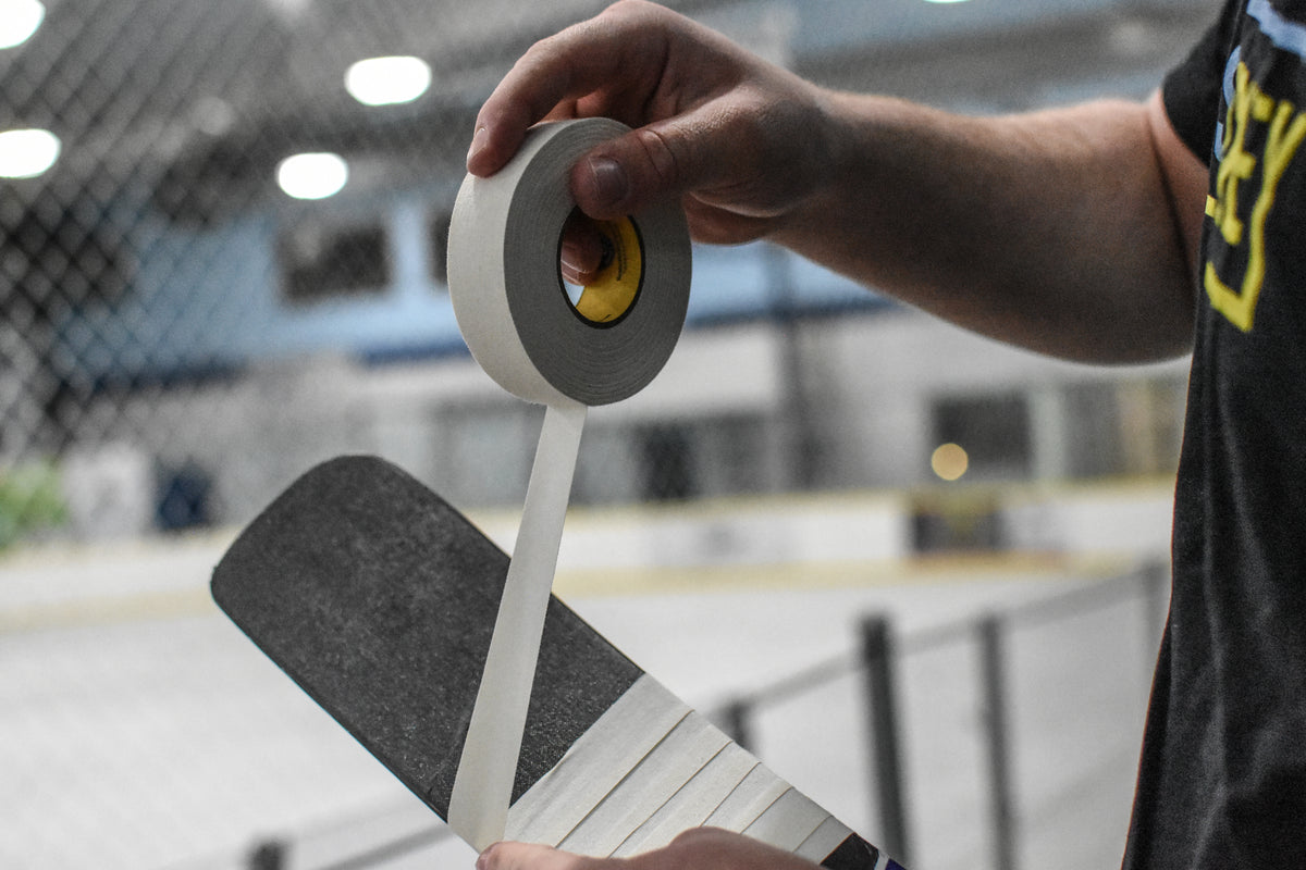 person appying white cloth tape to a goalie stick