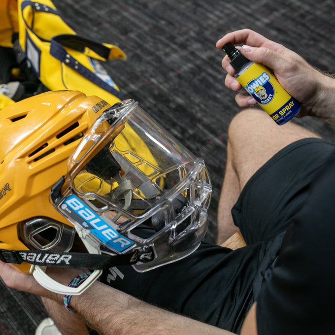 Person cleaning a yellow hockey helmet with a spray bottle on a dark textured surface