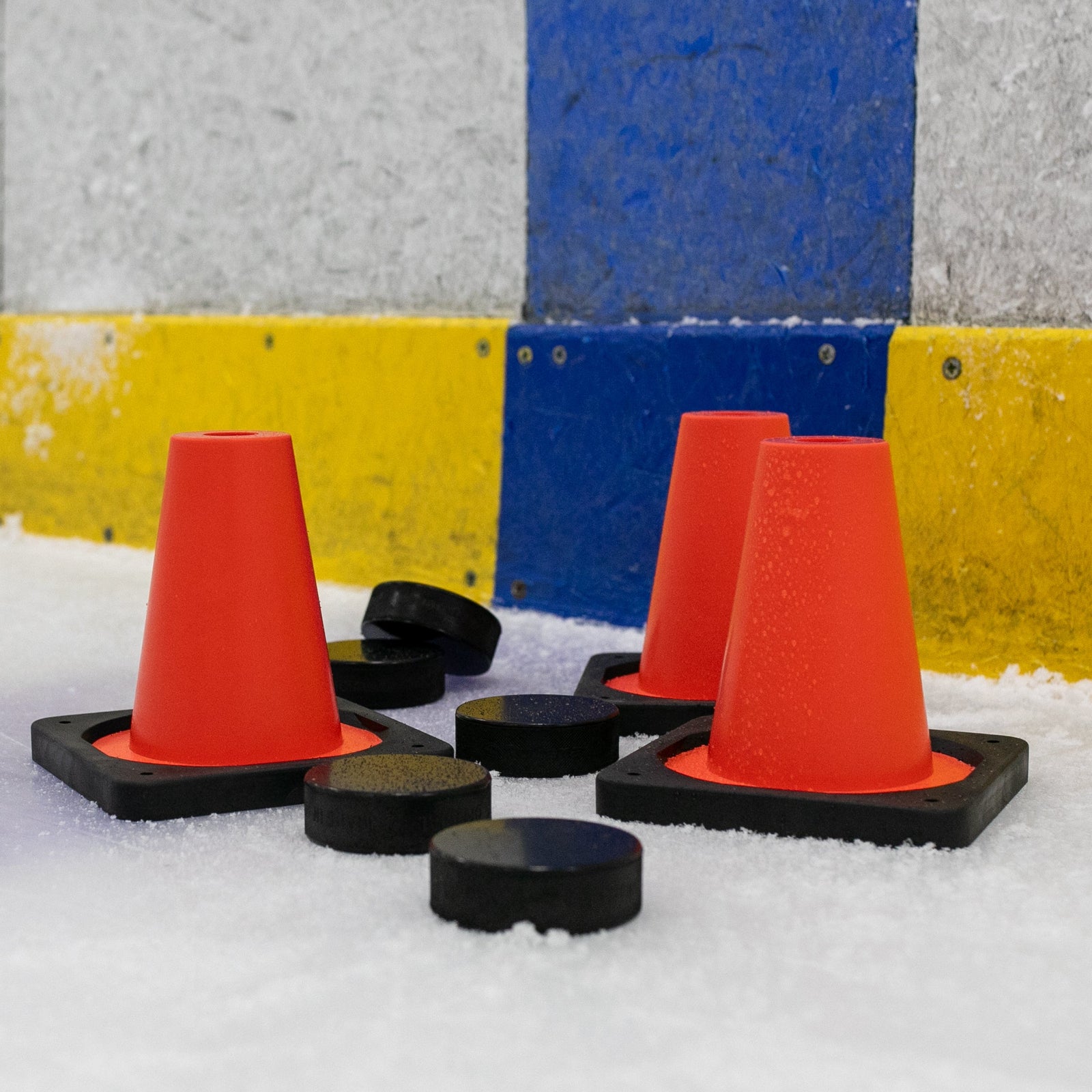 Orange cones on a snowy surface with a blue and yellow wall in the background.