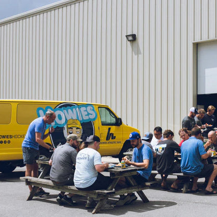 Group of people sitting around a picnic table outside a building with a Howies van in the background.