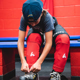 Person in hockey gear tying skates in front of a red wall with blue bench