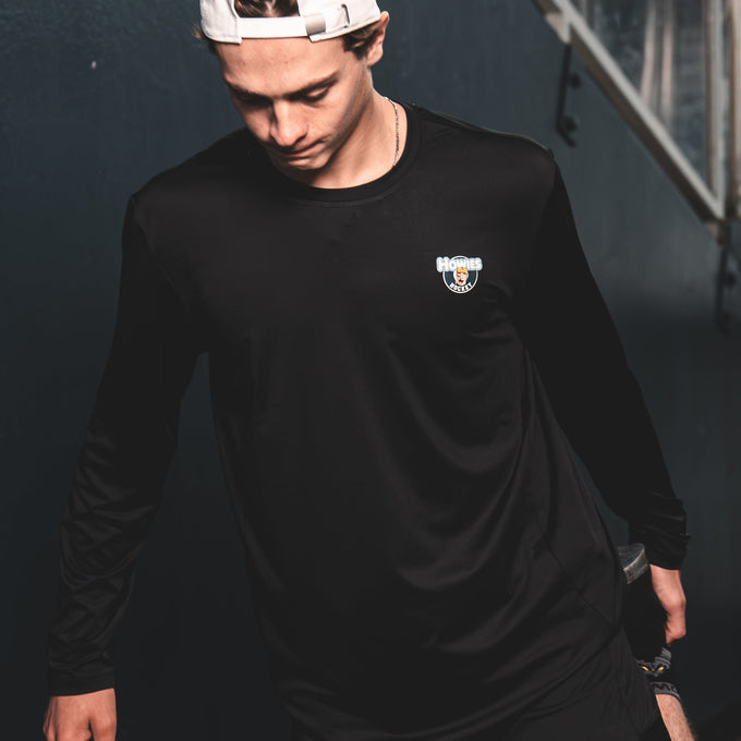 Person wearing a black long-sleeve shirt and shorts with a logo, standing against a dark background.