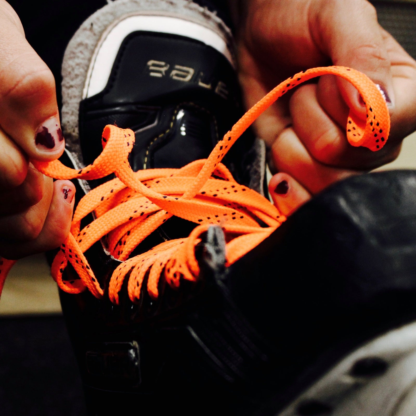 Person tying orange laces on black skates