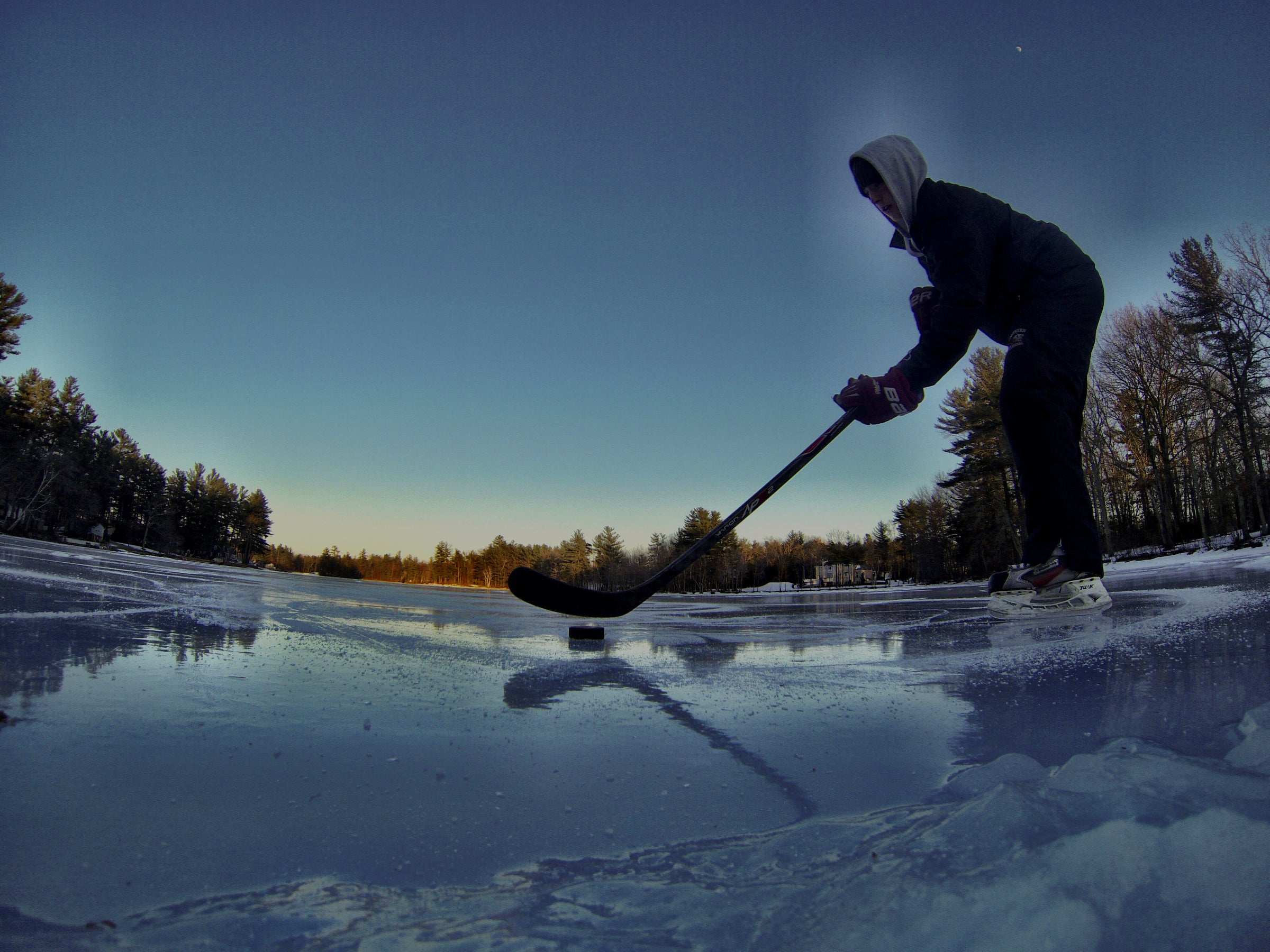 Person playing ice hockey on a frozen lake with trees in the background
