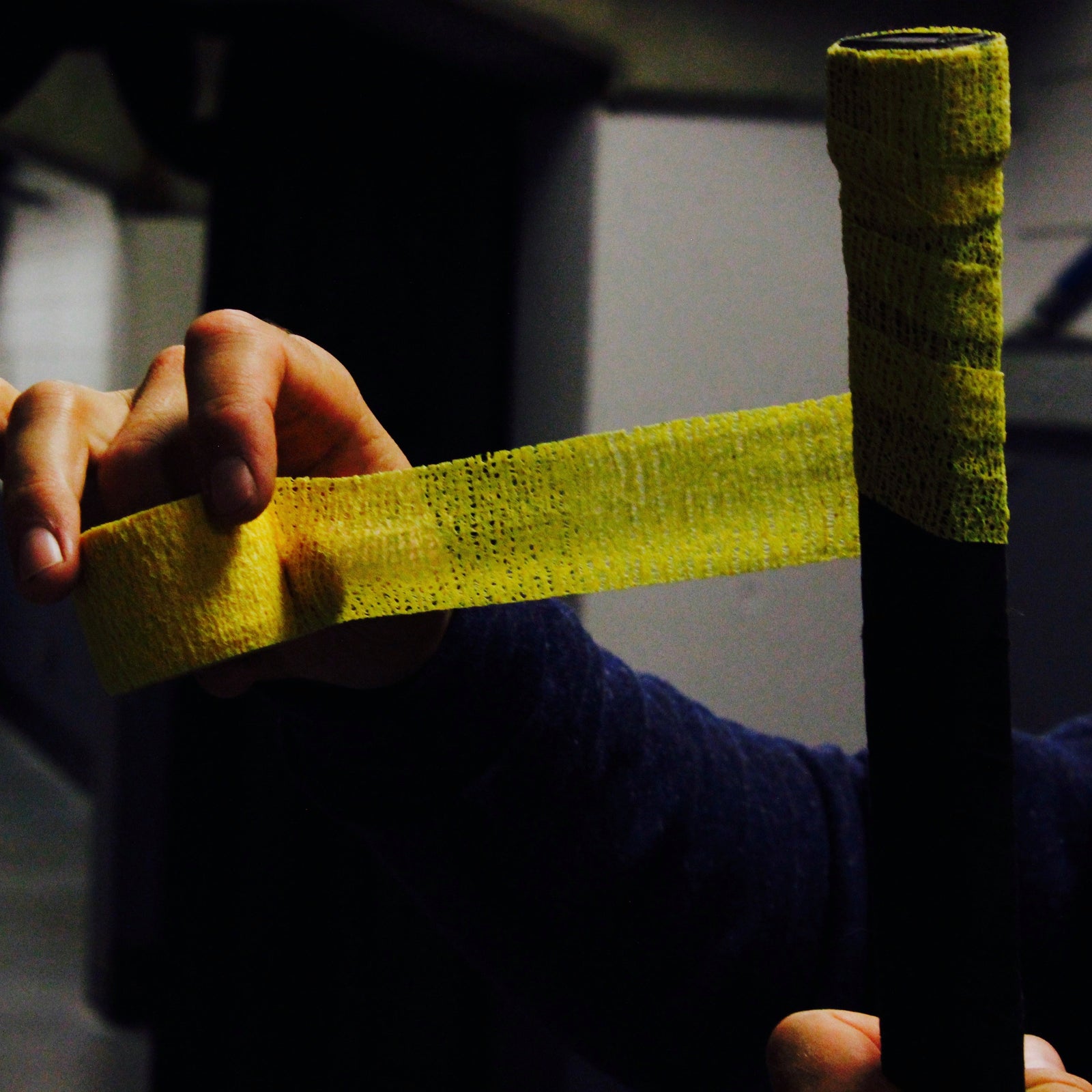 Hand holding a yellow tape wrapped around a black cylindrical object in an indoor setting.