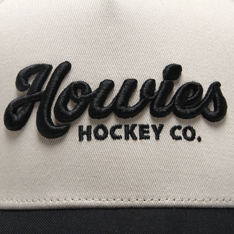 Close-up of the raised black embroidered Howies Hockey Co. script logo on the cream front panel of the Clean Sheet Lid