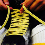 Person tying yellow shoelaces on a black hockey skate