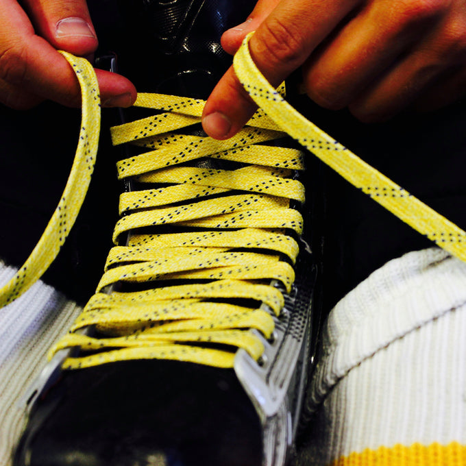 Person tying yellow shoelaces on a black hockey skate